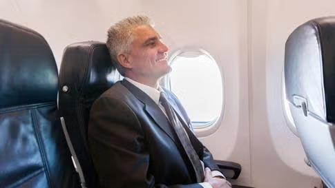 Man enjoying his airline seat Man working from an airline seat representing the perks of getting the best seats on the plane.